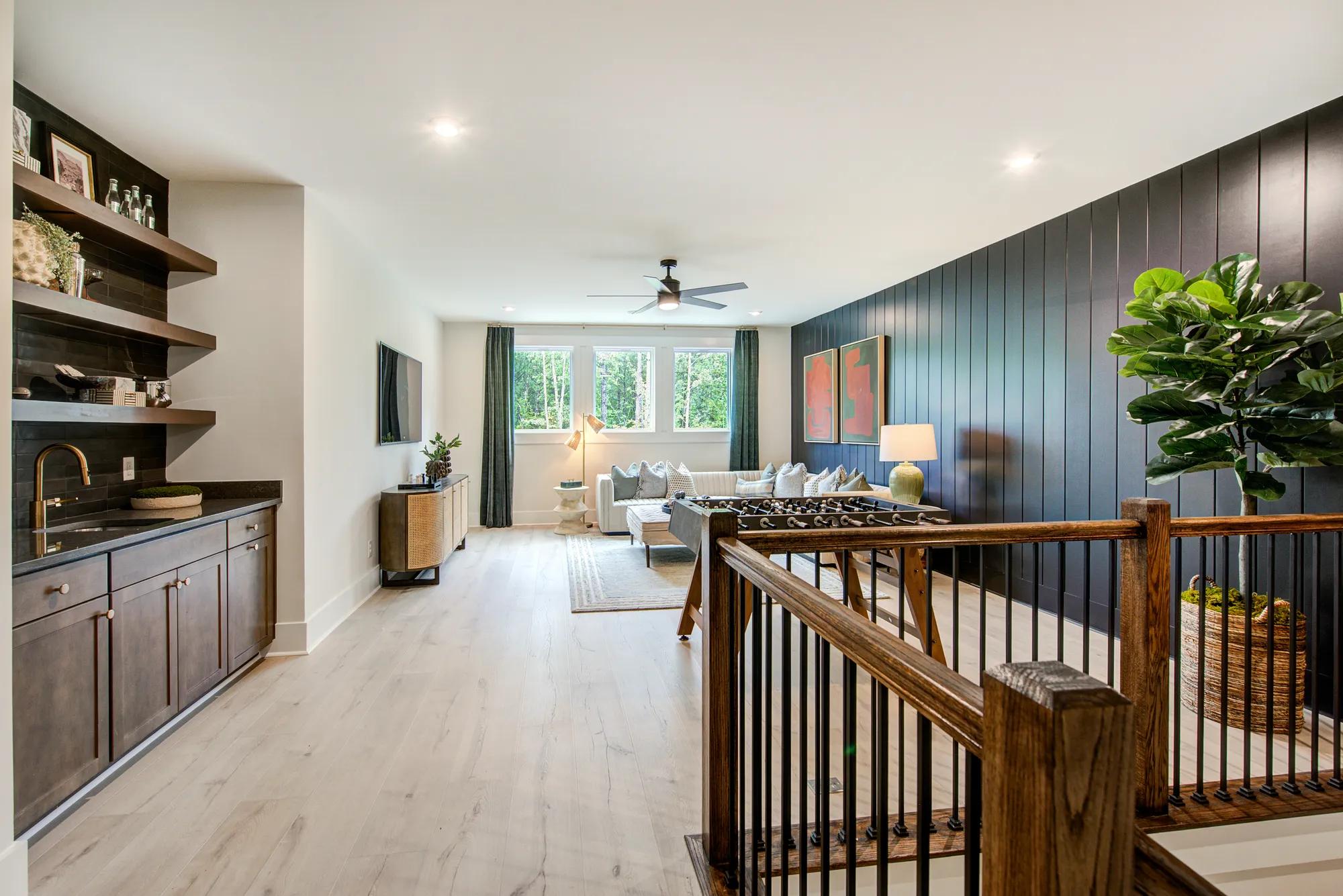 Custom home upstairs gameroom with hardwood floors, black panel accent wall, and rich wood wet bar