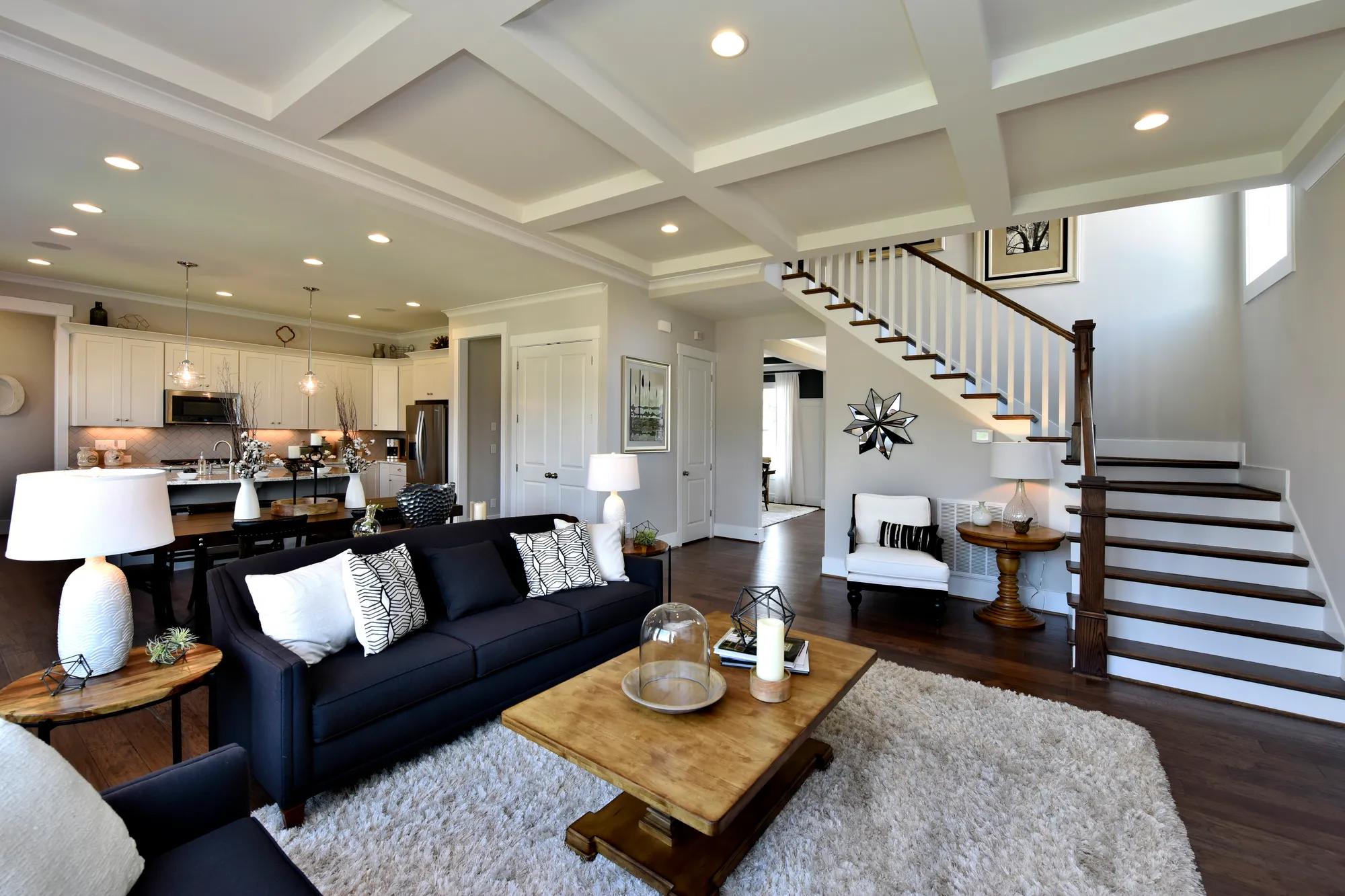 Living room with dark hardwood floors, and stained staircase, coffered ceiling, and recessed lights