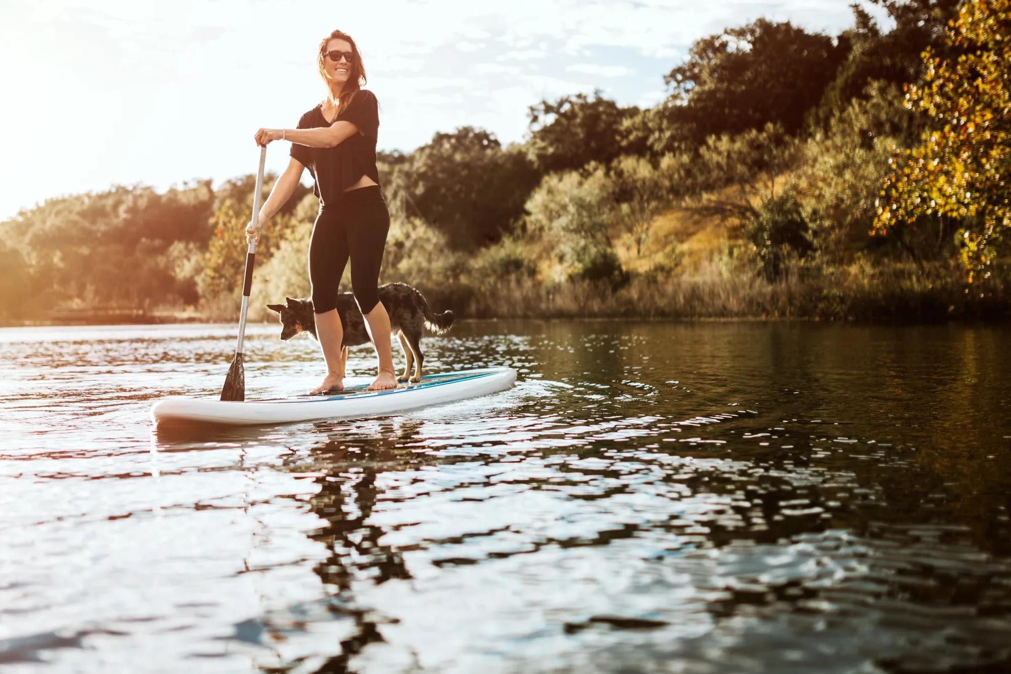 Young woman and dog enjoying paddle boarding on lake