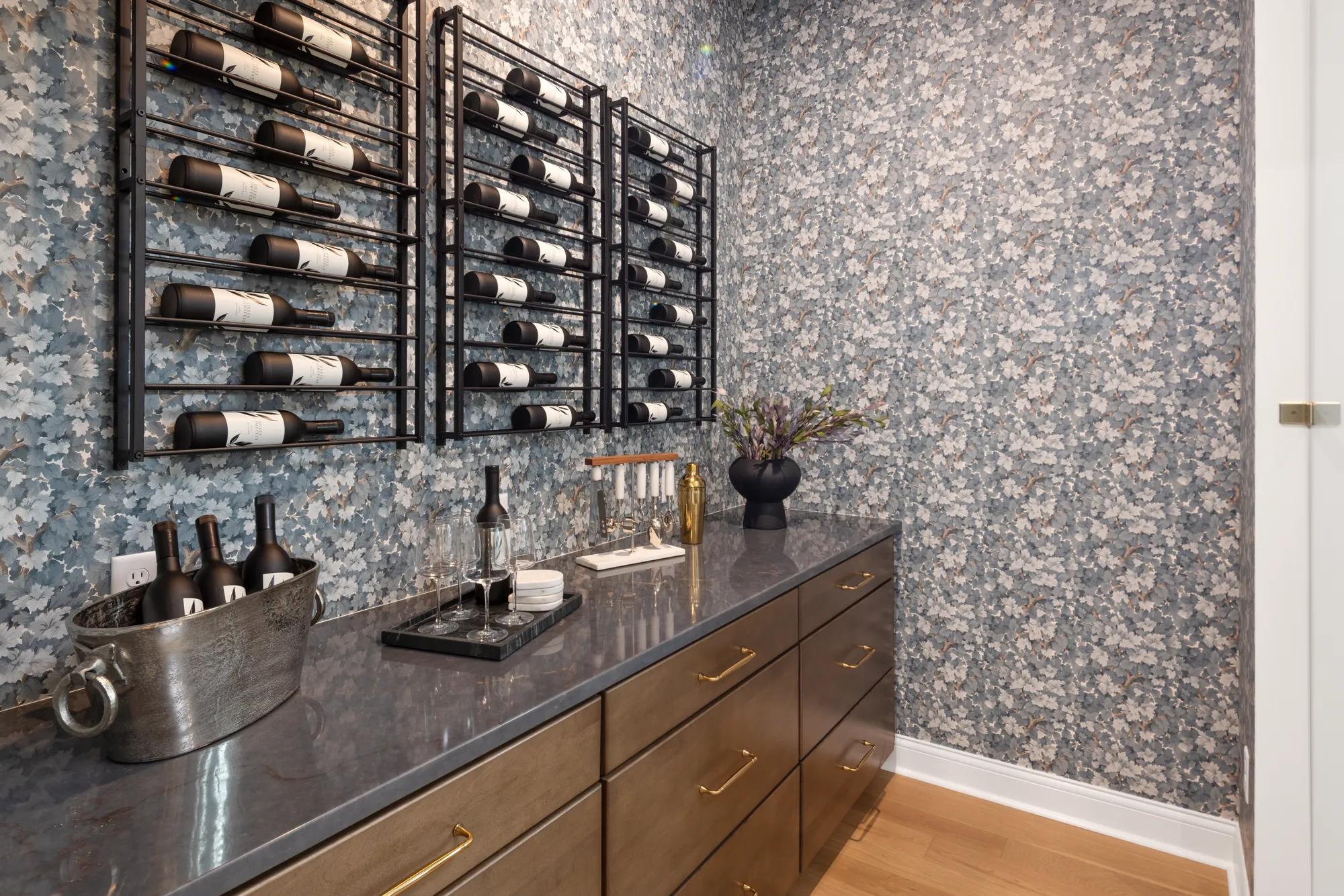 Custom home wine room with dark wood cabinets, dark countertops, and wallpaper