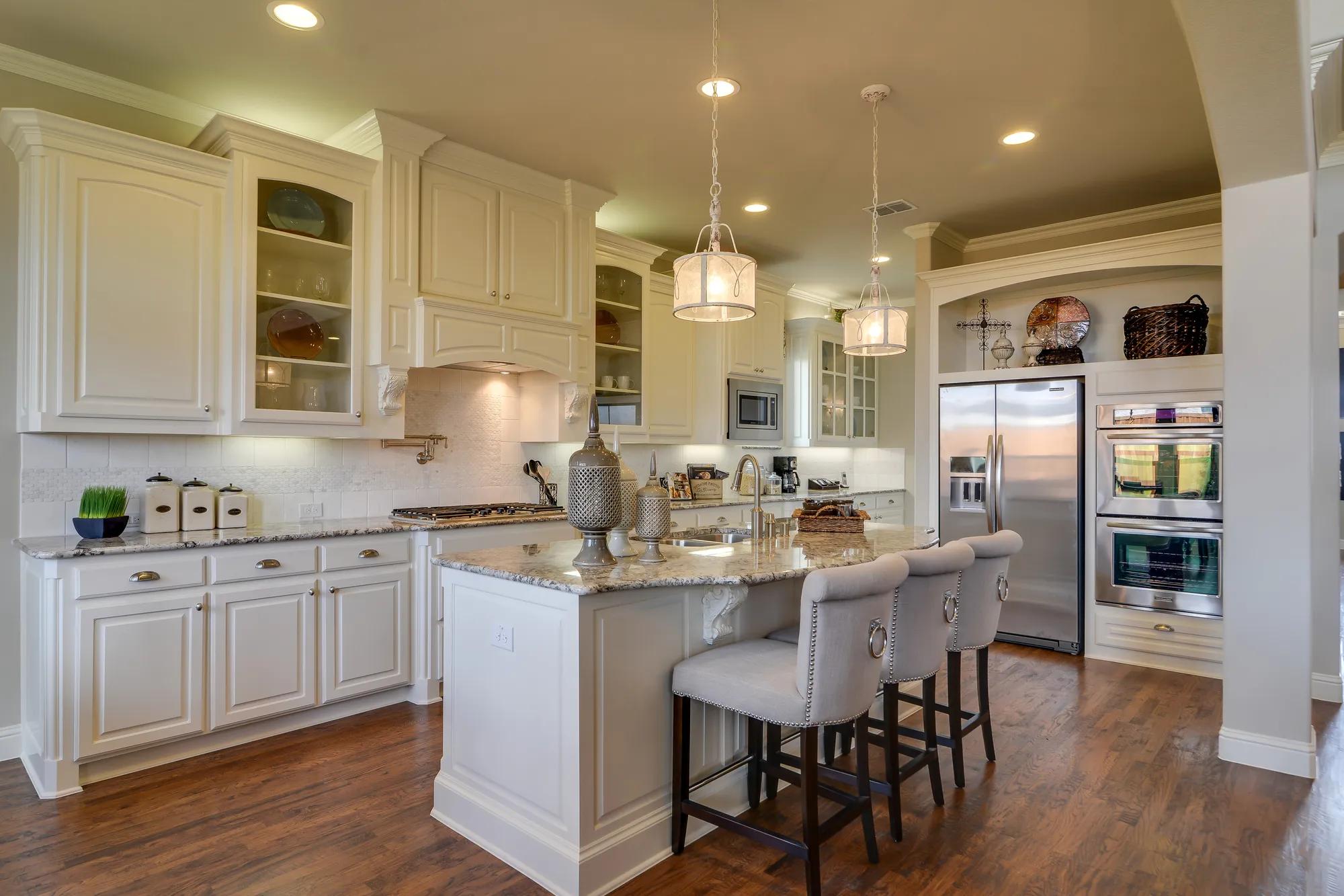 Kitchen with island, granite countertop, pendant lighting, stainless steel appliances, arched opening, wood range hood, backsplash, granite countertop, glass front cabinets