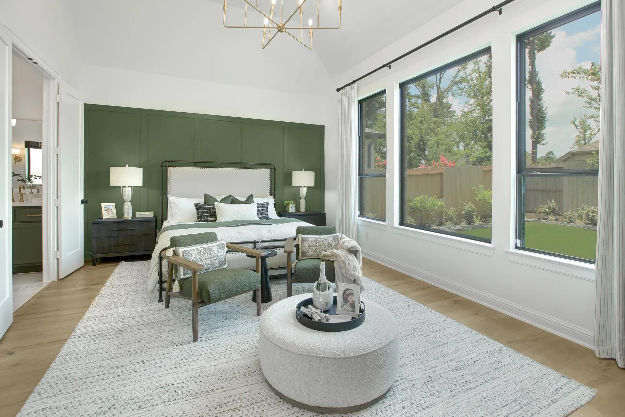 Custom home primary suite bedroom with green accent wall and wall of windows