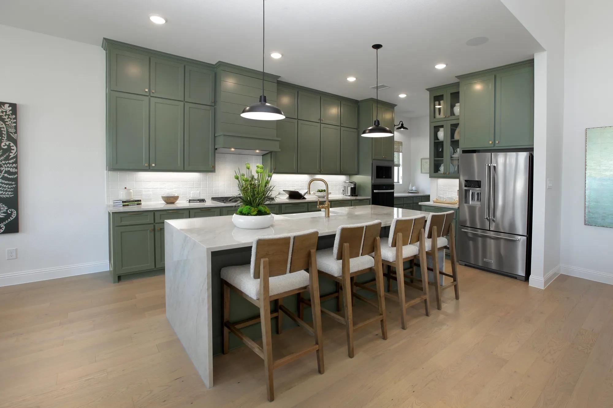 Custom home kitchen with green cabinets, light hardwood floor and waterfall island