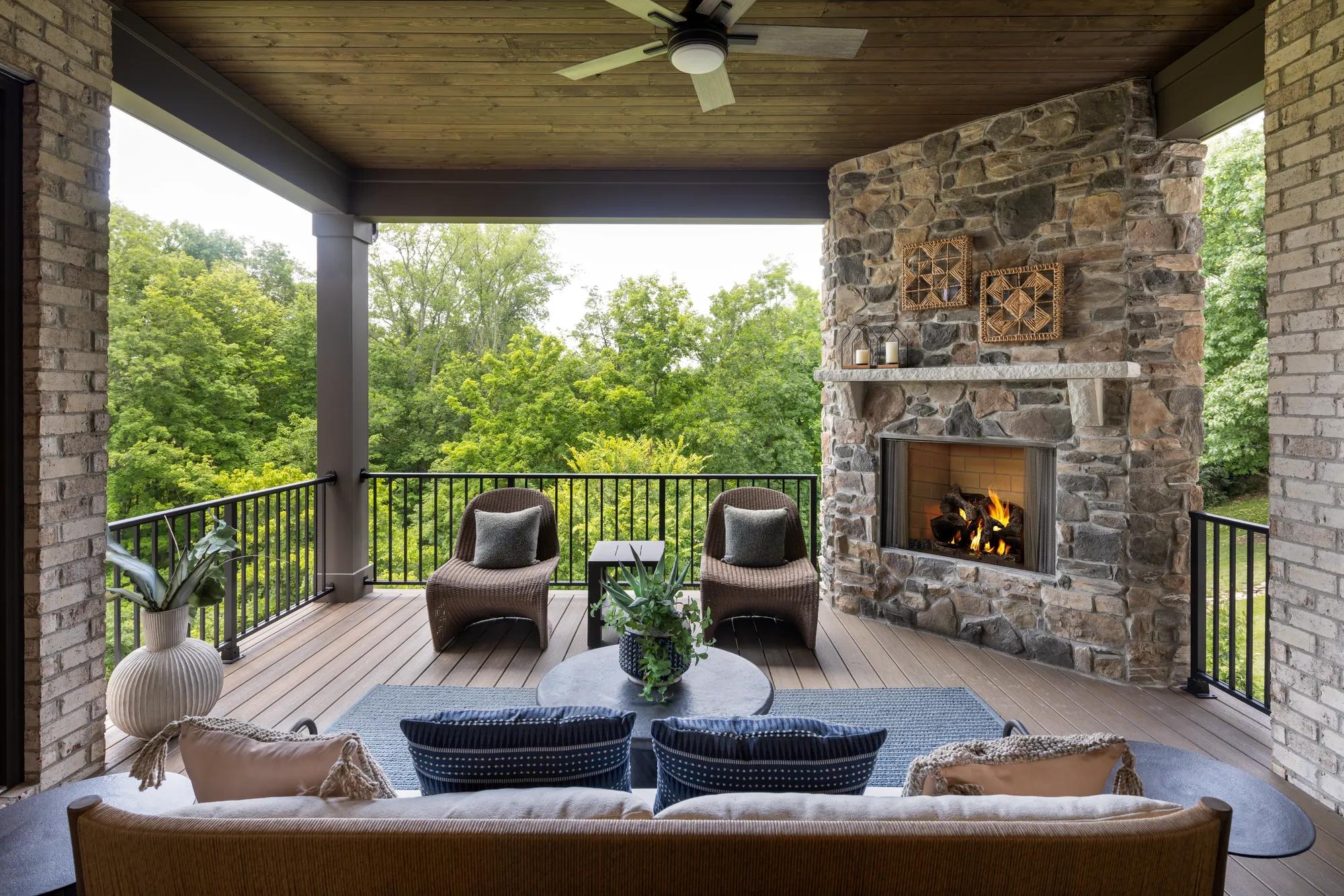 Custom home covered porch with stone fireplace overlooking the woods