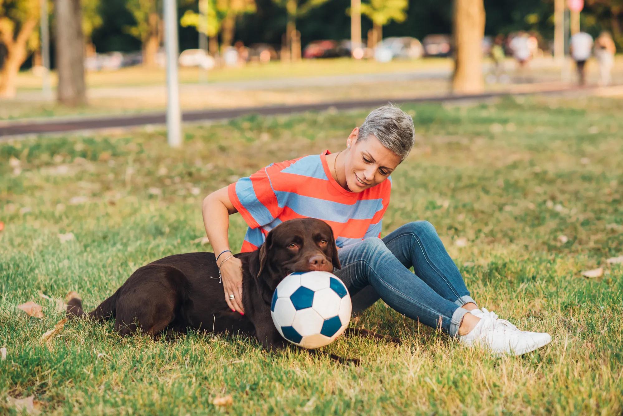woman and dog with soccer ball in park