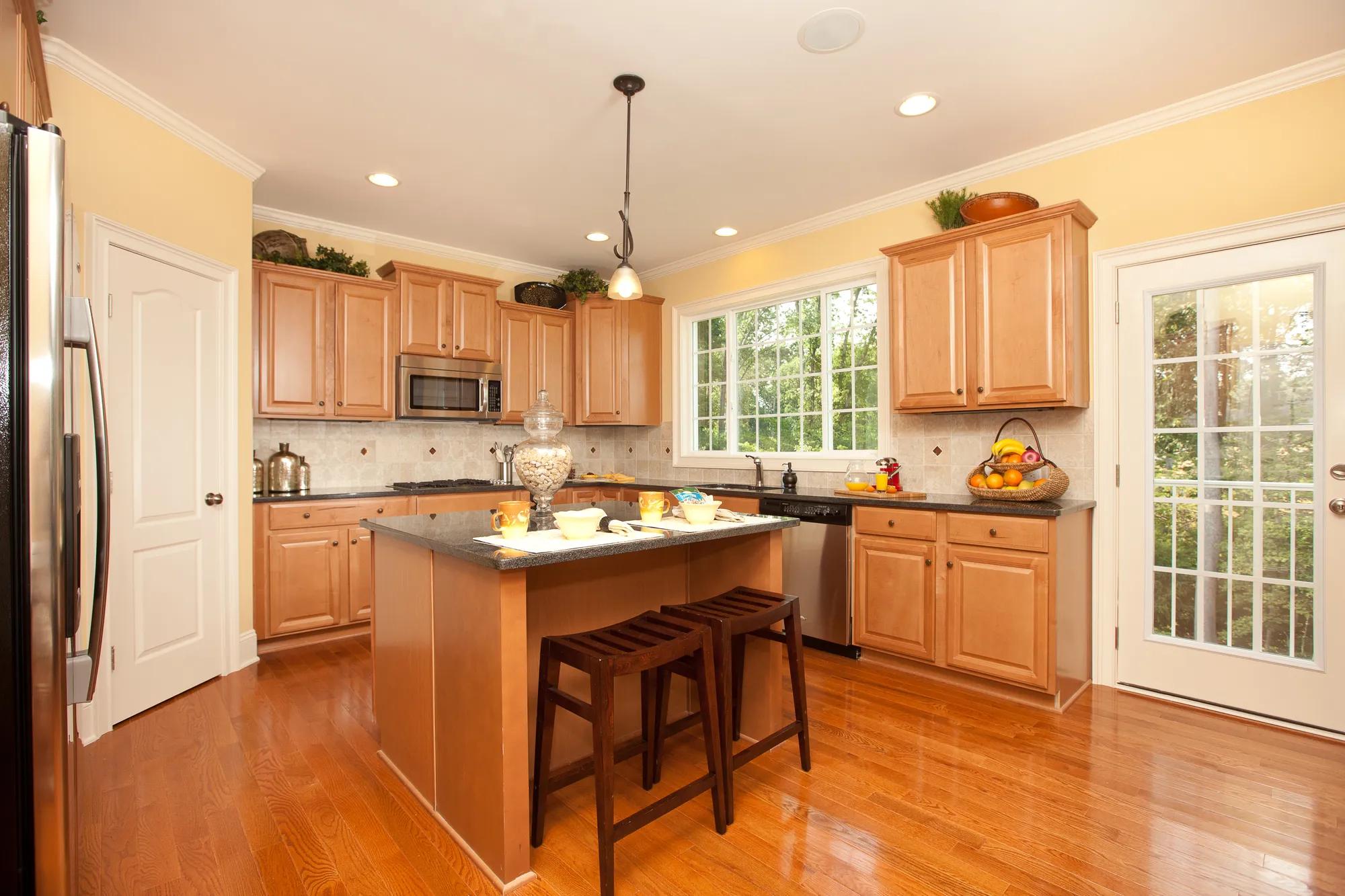 Kitchen with light hardwood floor, light wood cabinets, stainless steel appliances, tile backsplash, island, pendant lighting, accent lighting, ceiling accent, yellow decor