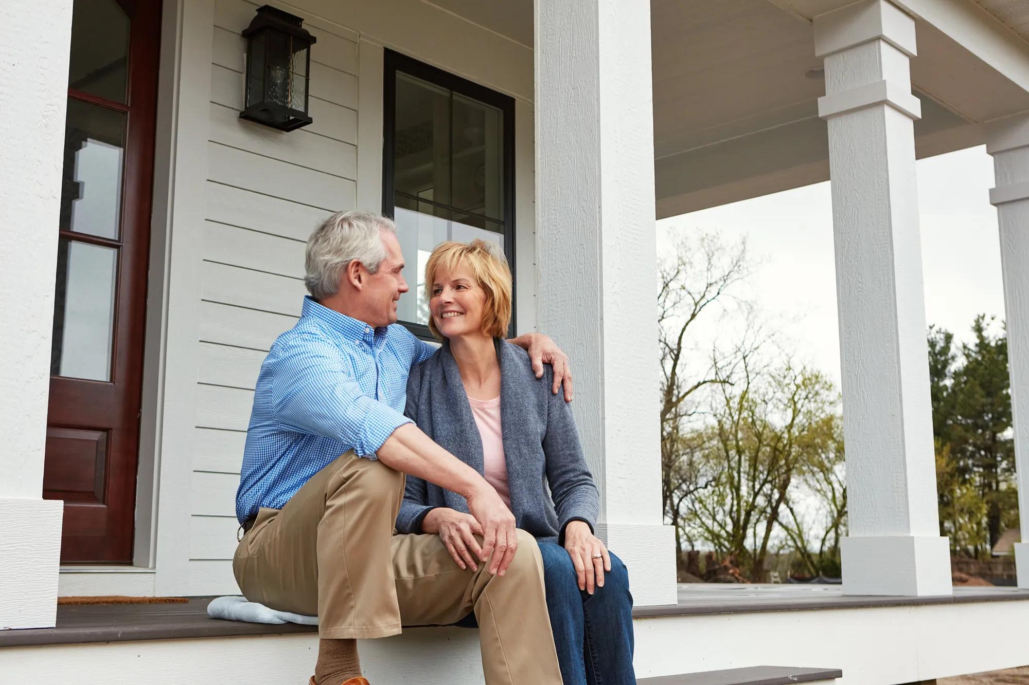 Happy couple sitting in front of home
