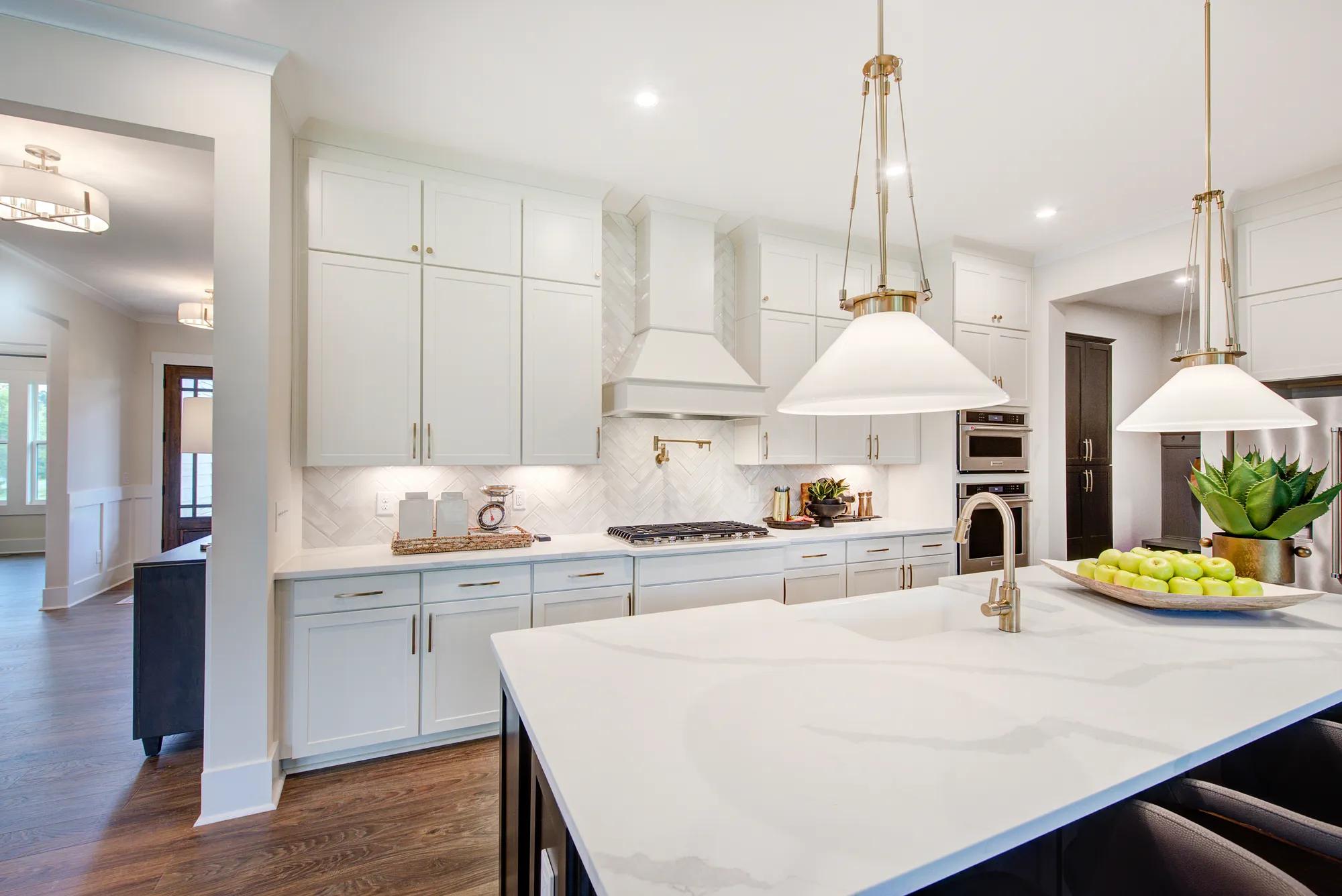 Custom home kitchen with white backsplash, countertops, and cabinets with gold finishes