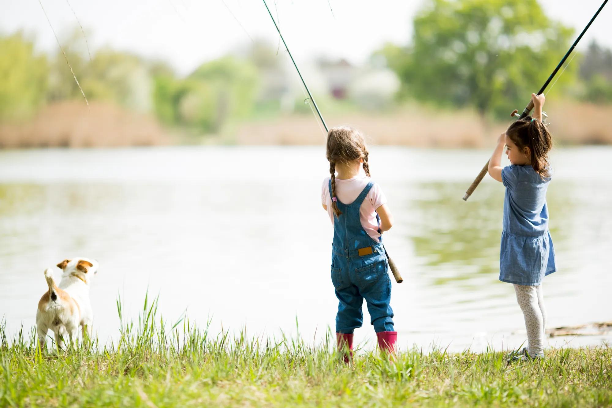 Two little girls and dog fishing at pond