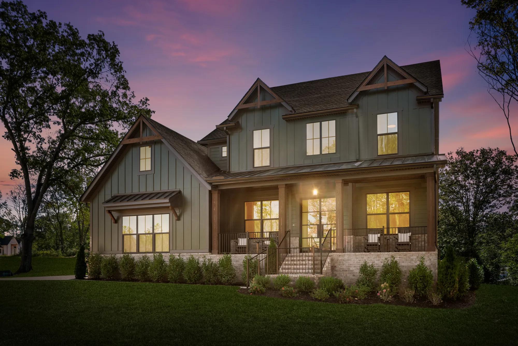 Green new construction home exterior with covered front porch at sunset 
