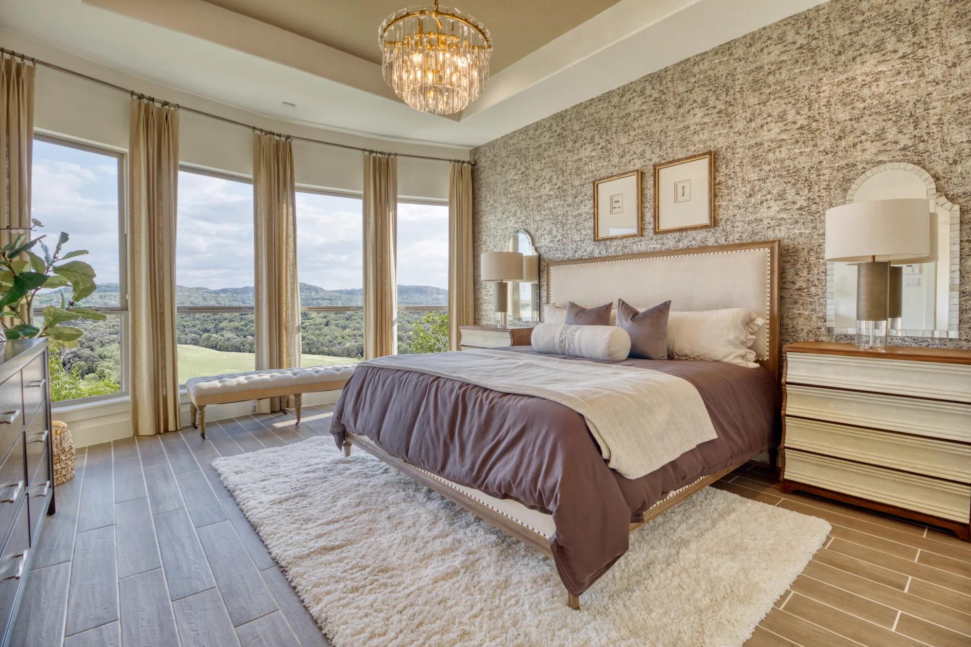 Custom home primary suite bedroom with bay windows, painted tray ceiling, and wallpaper accent wall