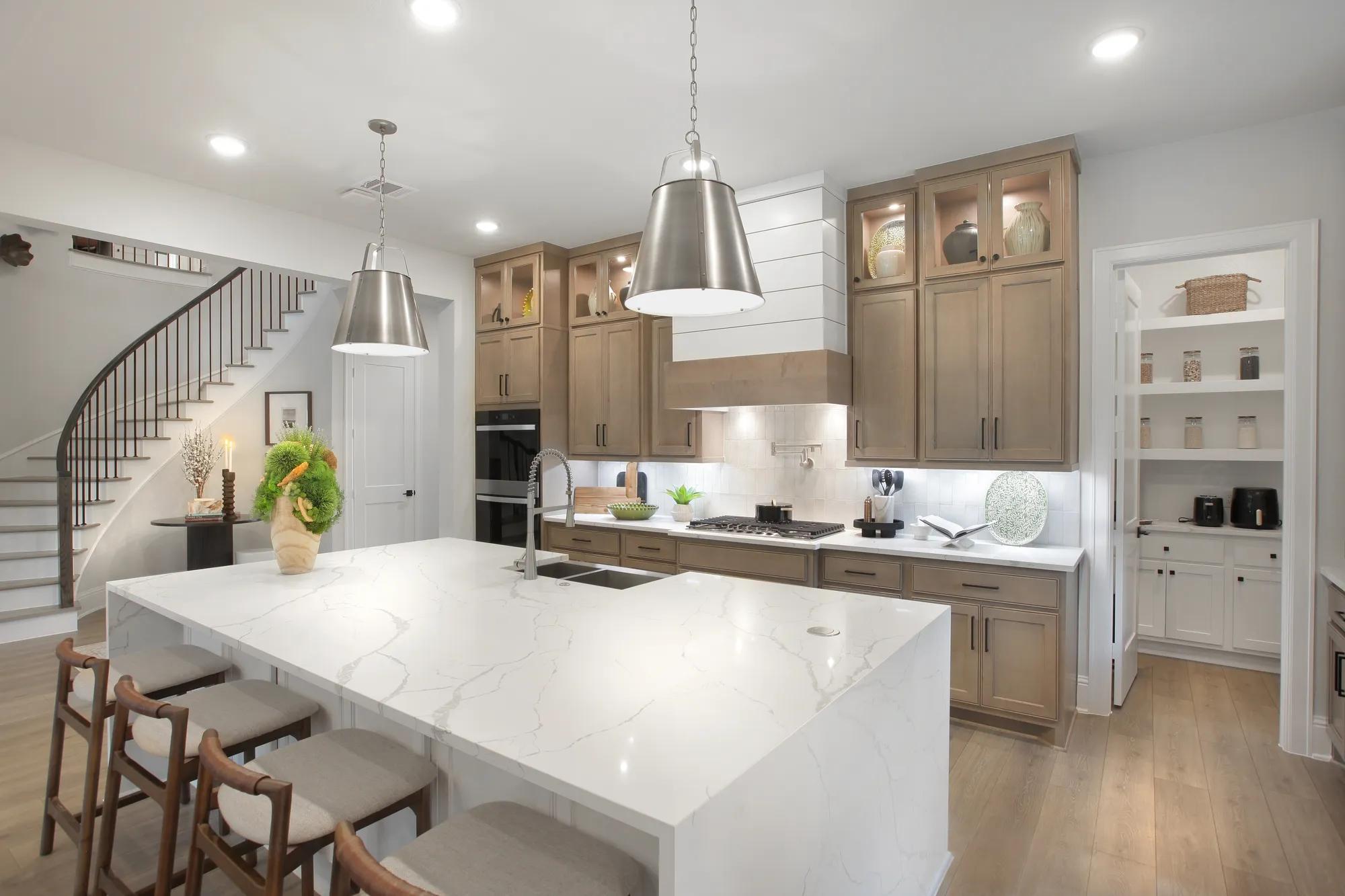 Custom home kitchen with light wood cabinets, white waterfall island, and working pantry