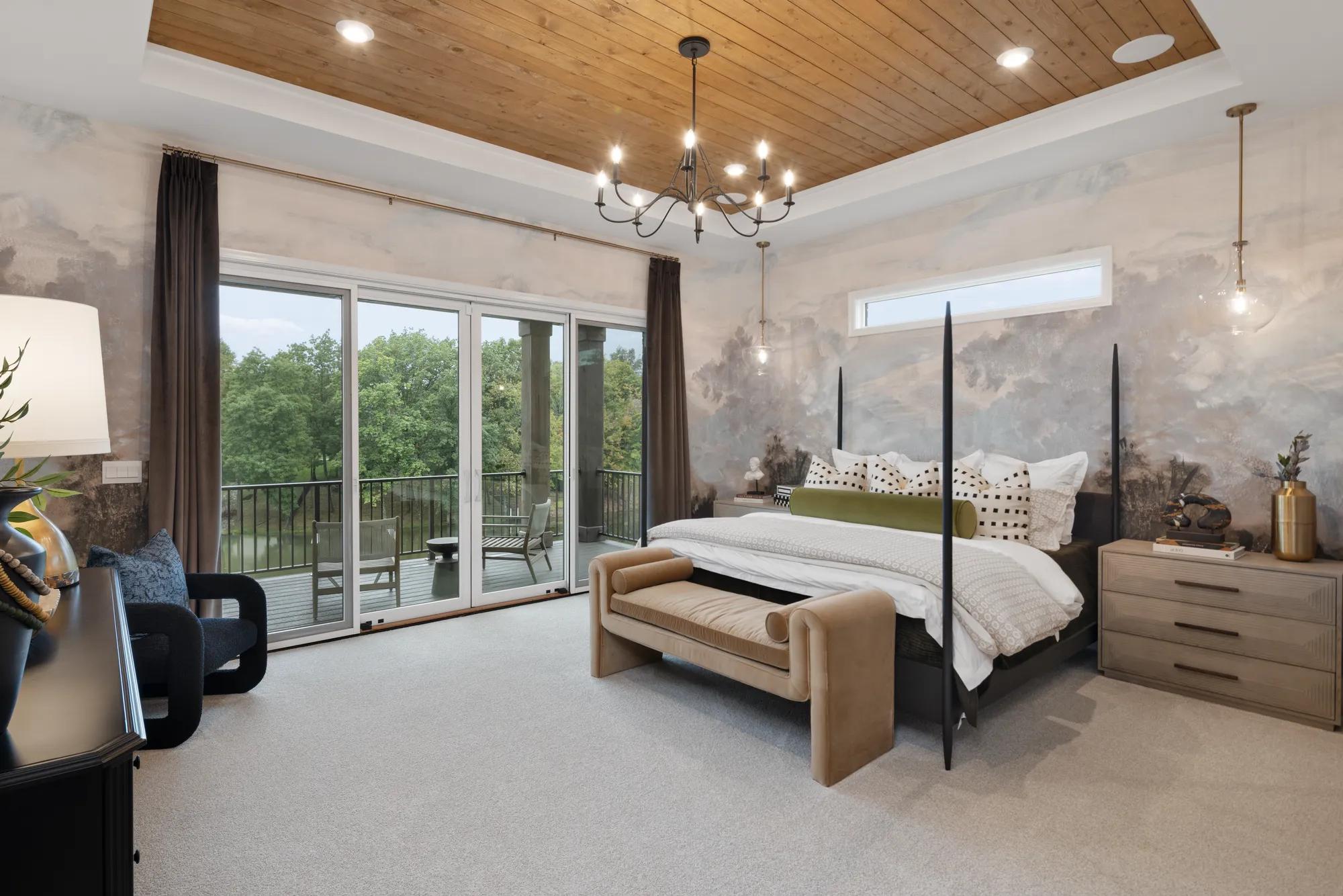 Custom home primary suite bedroom with wood panel ceiling and sliding glass door to balcony 