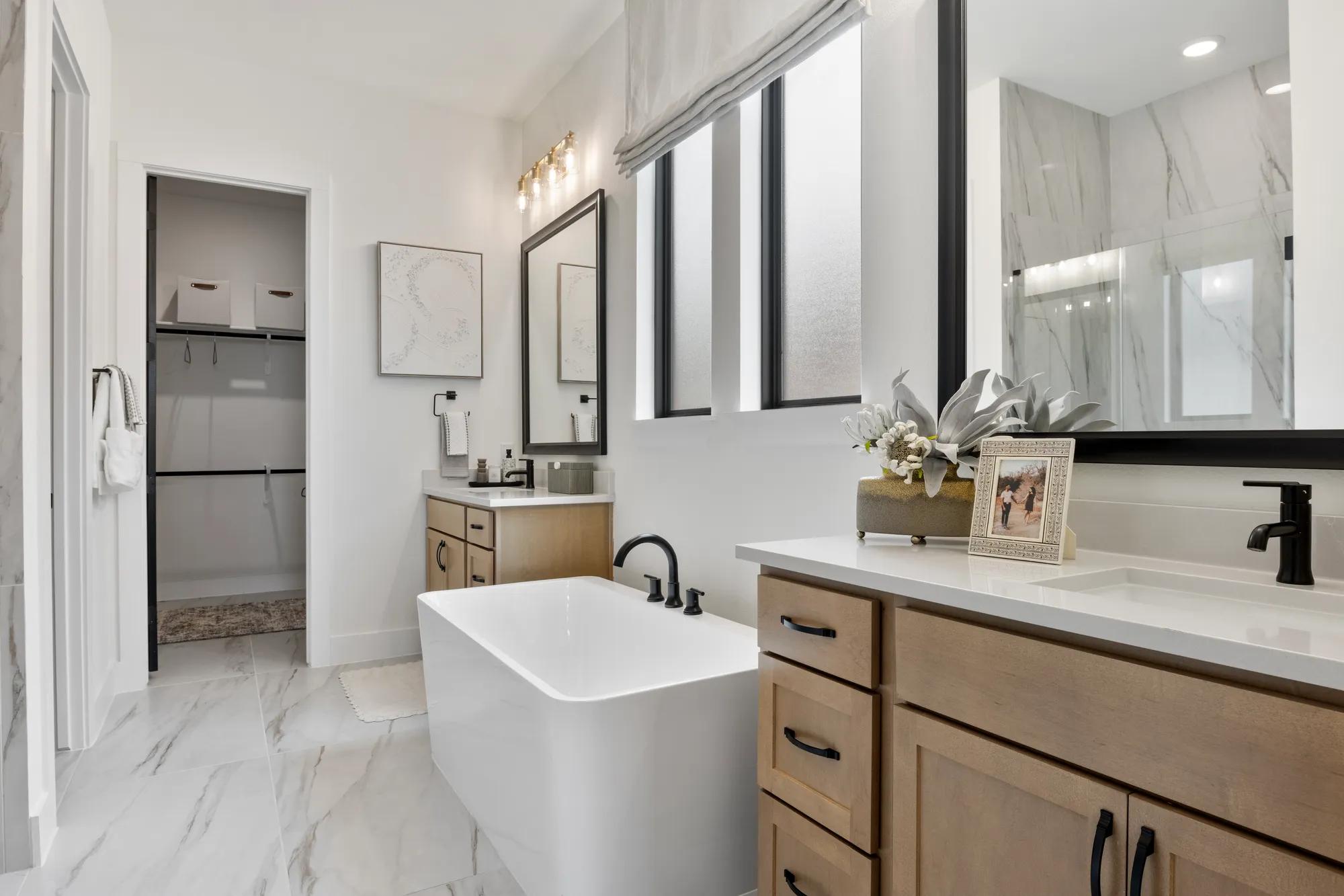 New home primary bathroom with double vanities, freestanding tub, and walk-in closet