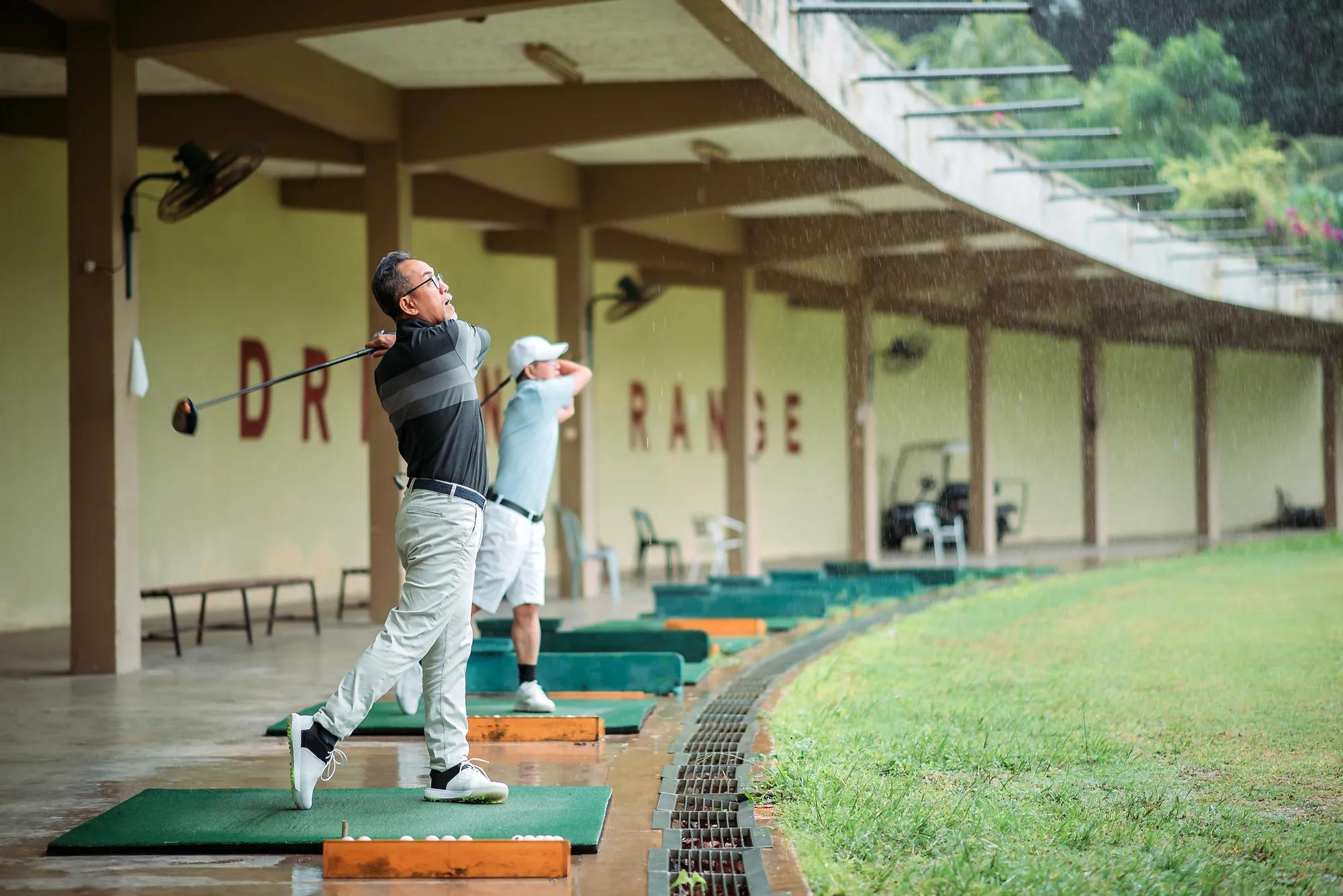 Two men swinging at golf driving range on a rainy day
