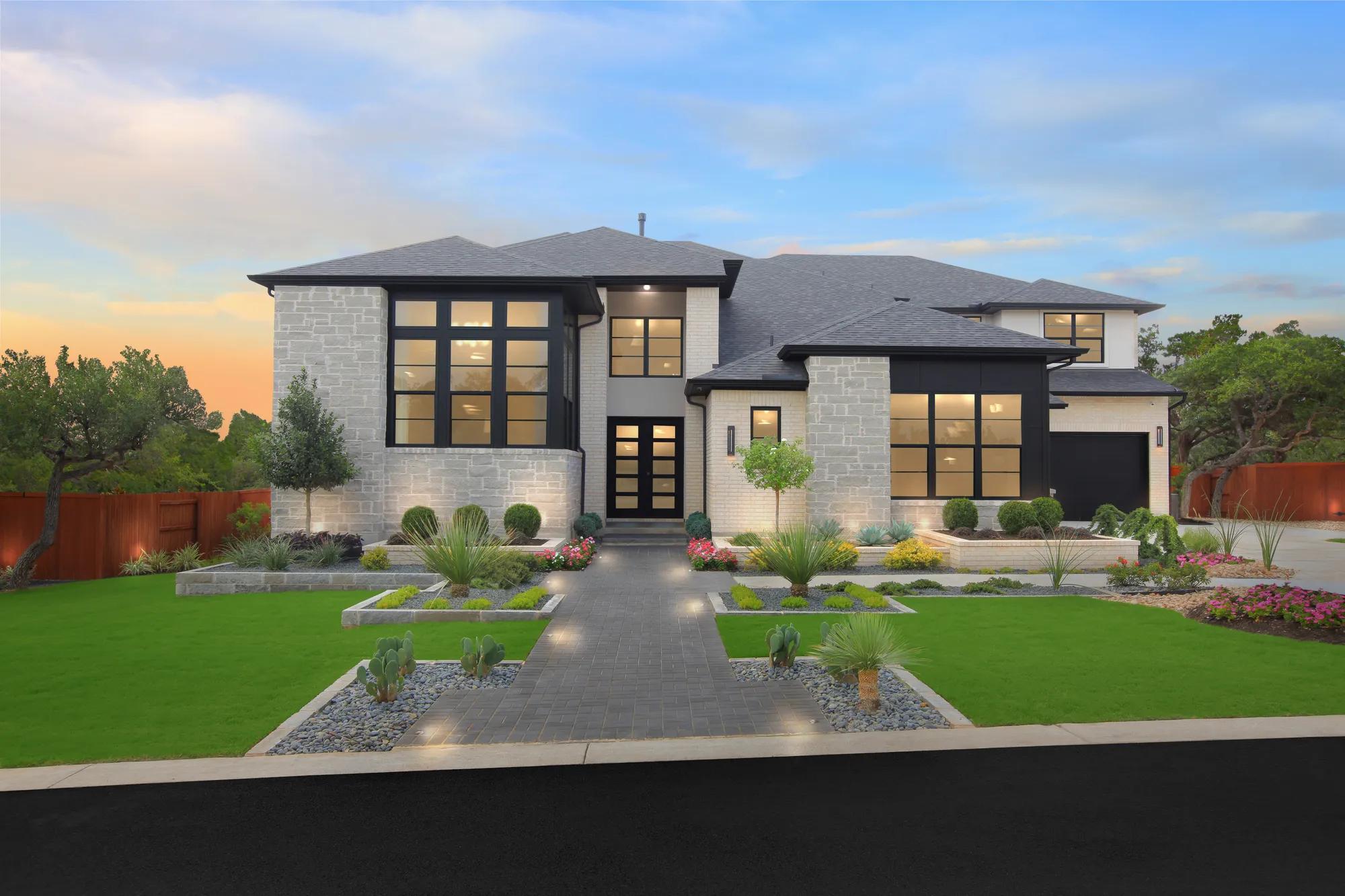 Stone and brick custom home exterior with black frame windows, and landscaped front yard, and fence at twilight