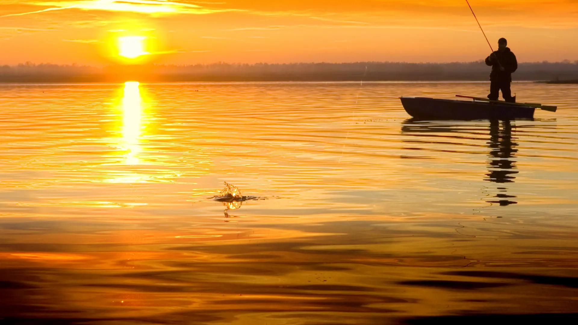 Man fishing in boat at sunset