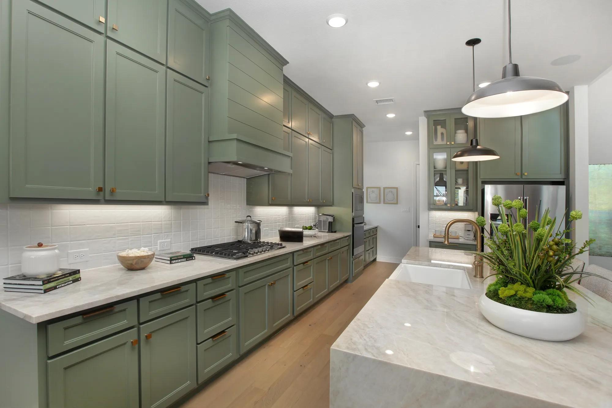Custom home kitchen with green cabinets, gold fixtures, tan countertops and waterfall island
