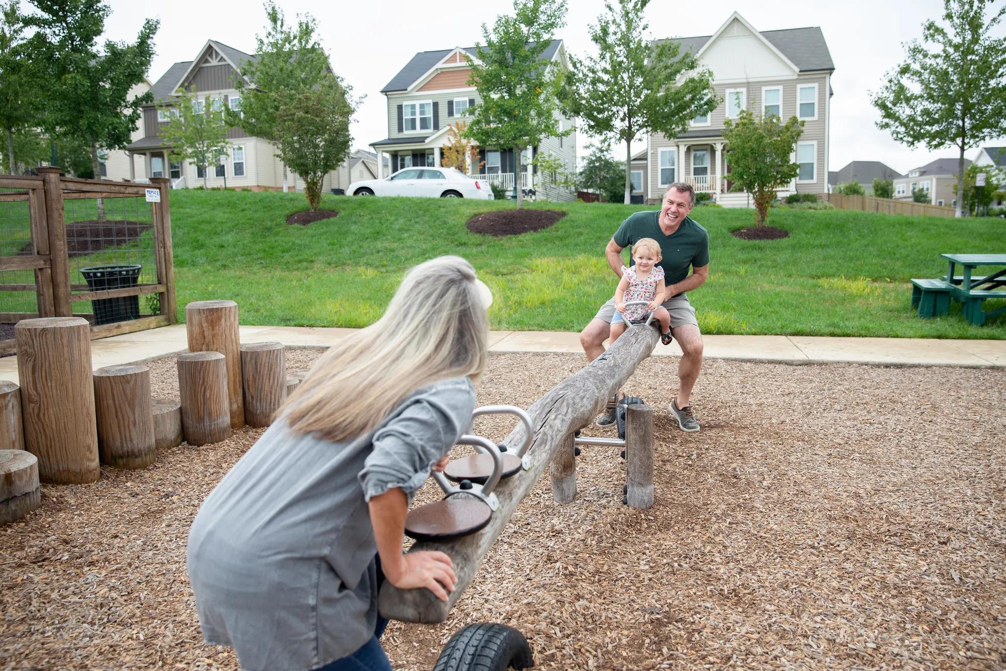 grandparents playing with grandchild in playground on seesaw
