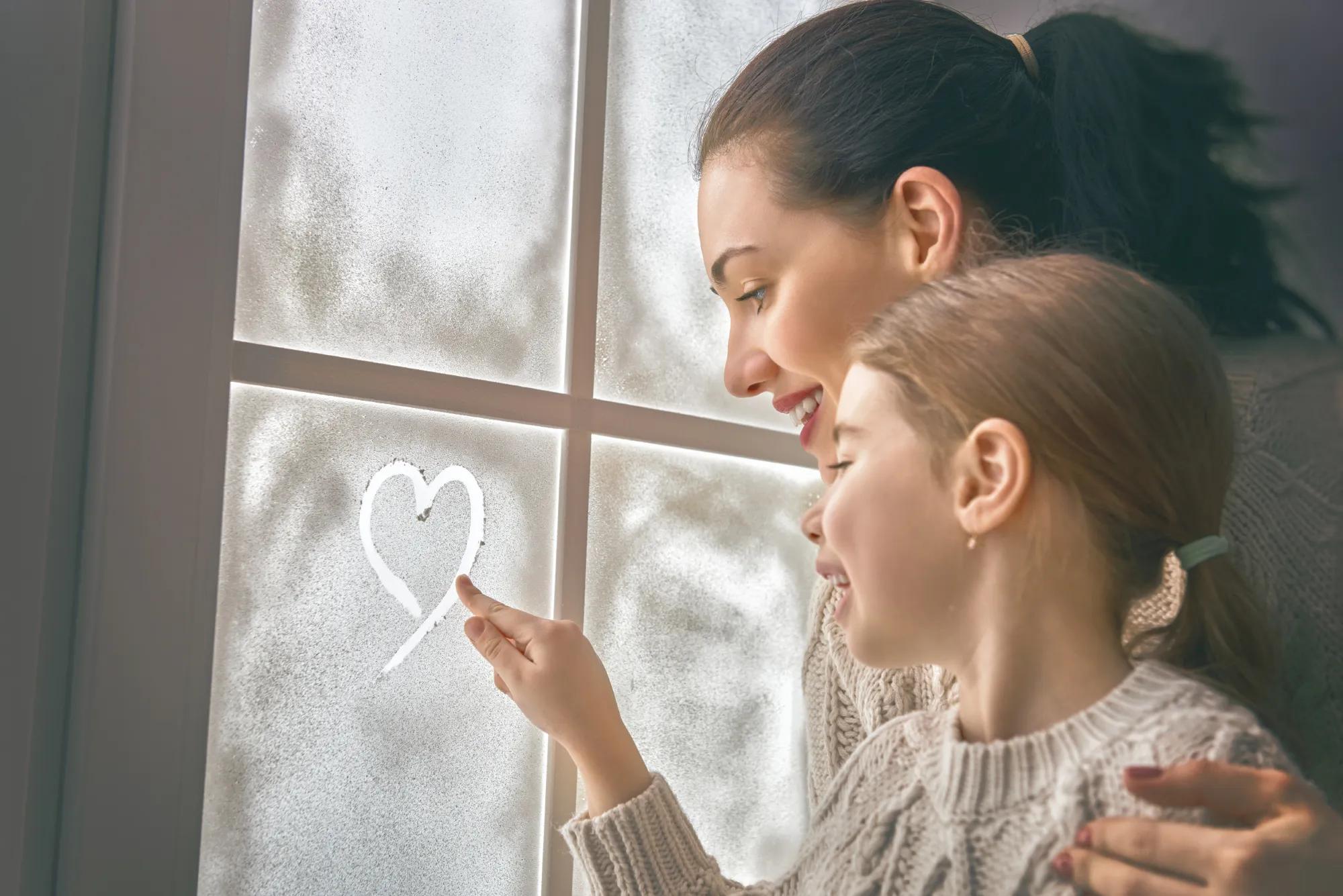 Mother and daughter drawing heart on window