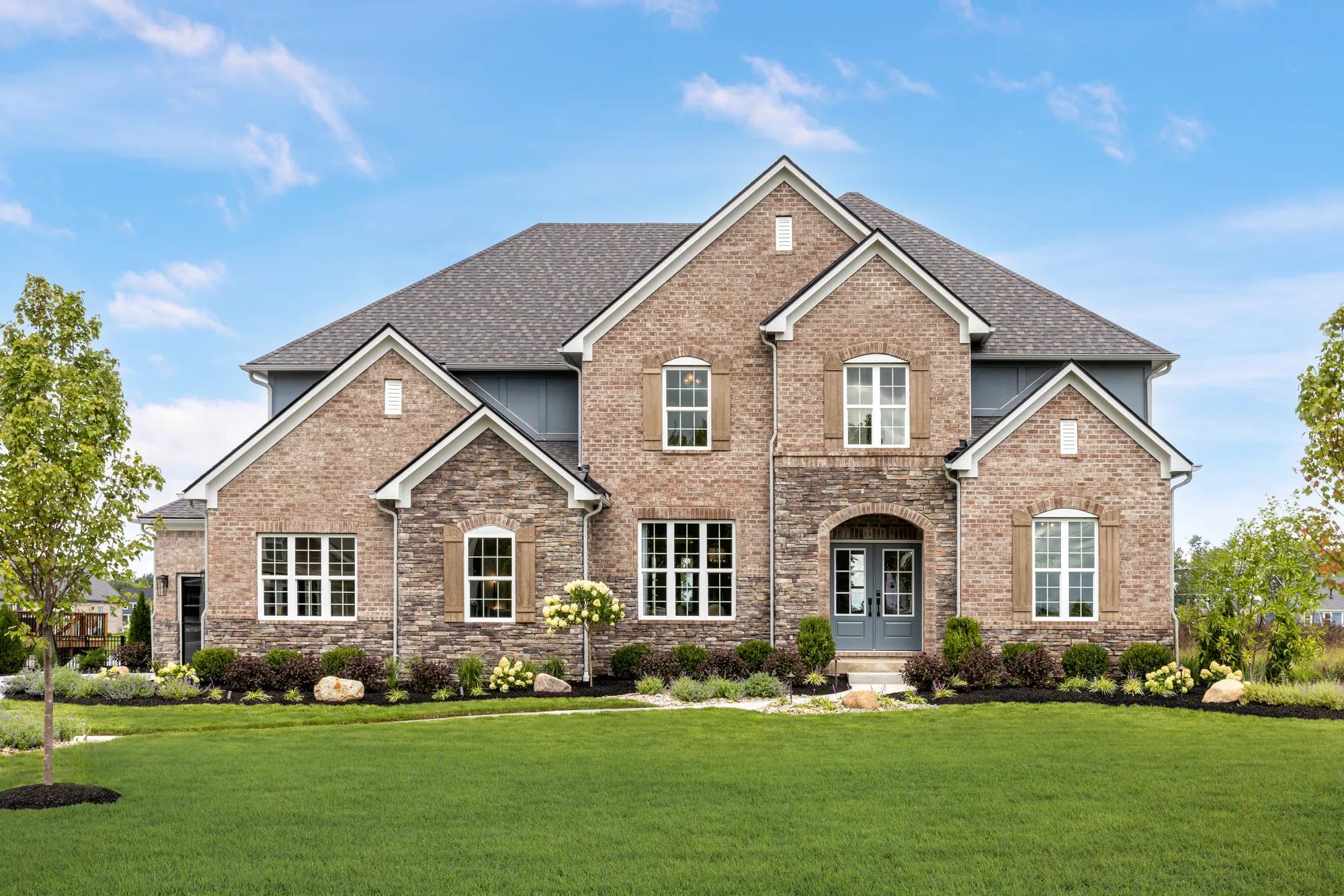 Classic brick and stone two-story home with blue front doors and arched front porch opening