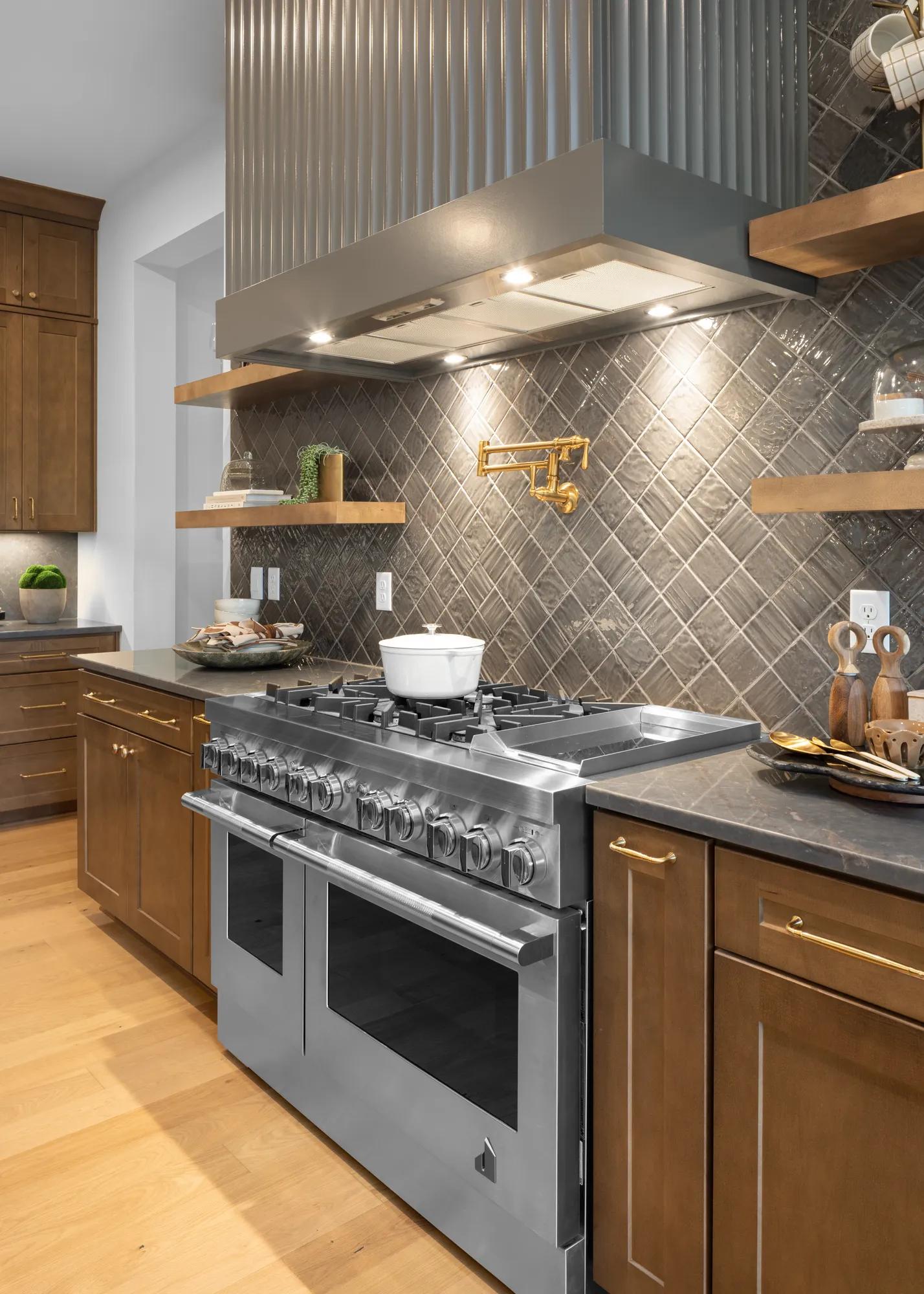 Custom home kitchen gas range with gold pot filler, tile wall backsplash, and floating shelves