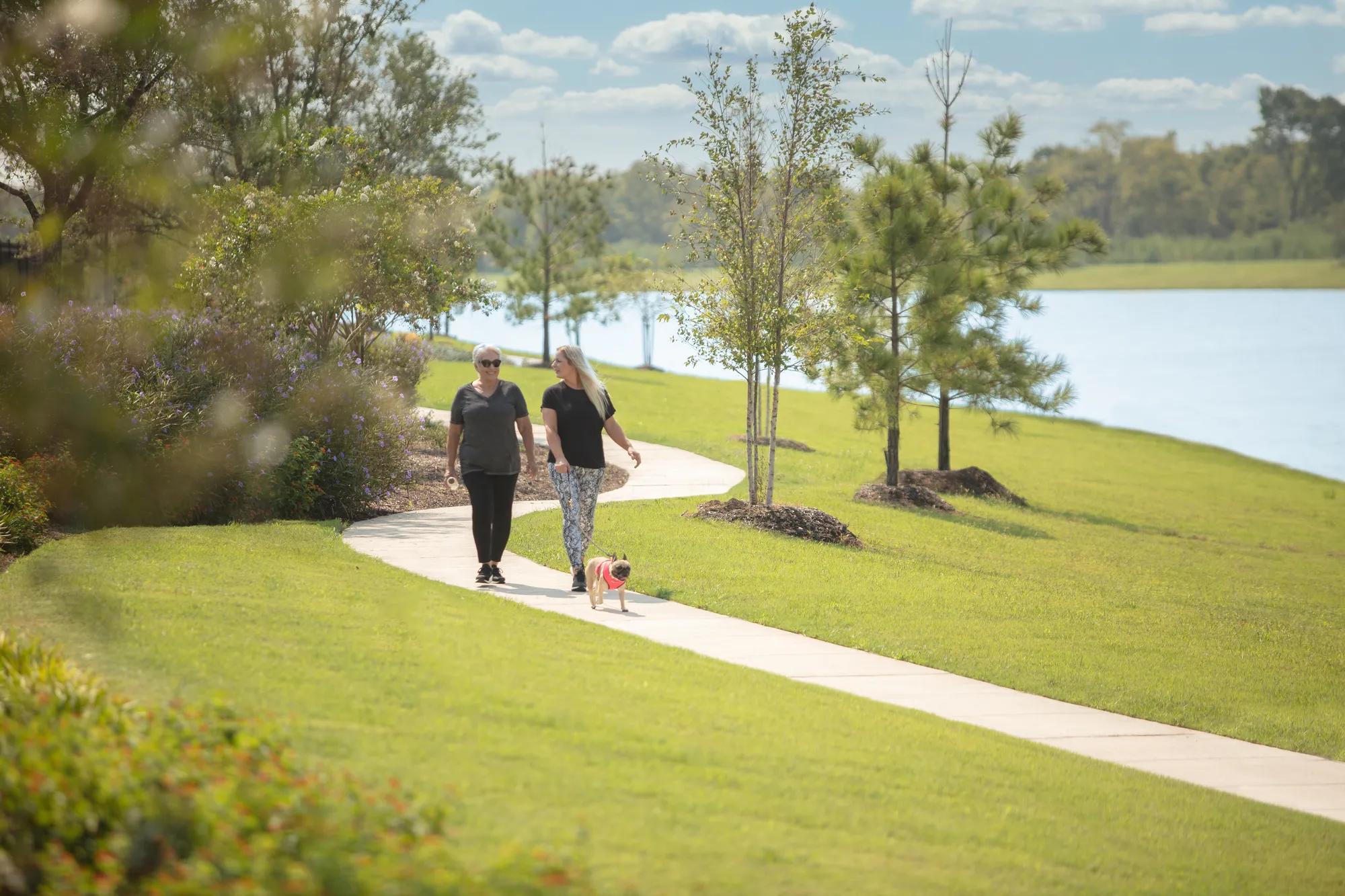 Two women walking dog on park trail