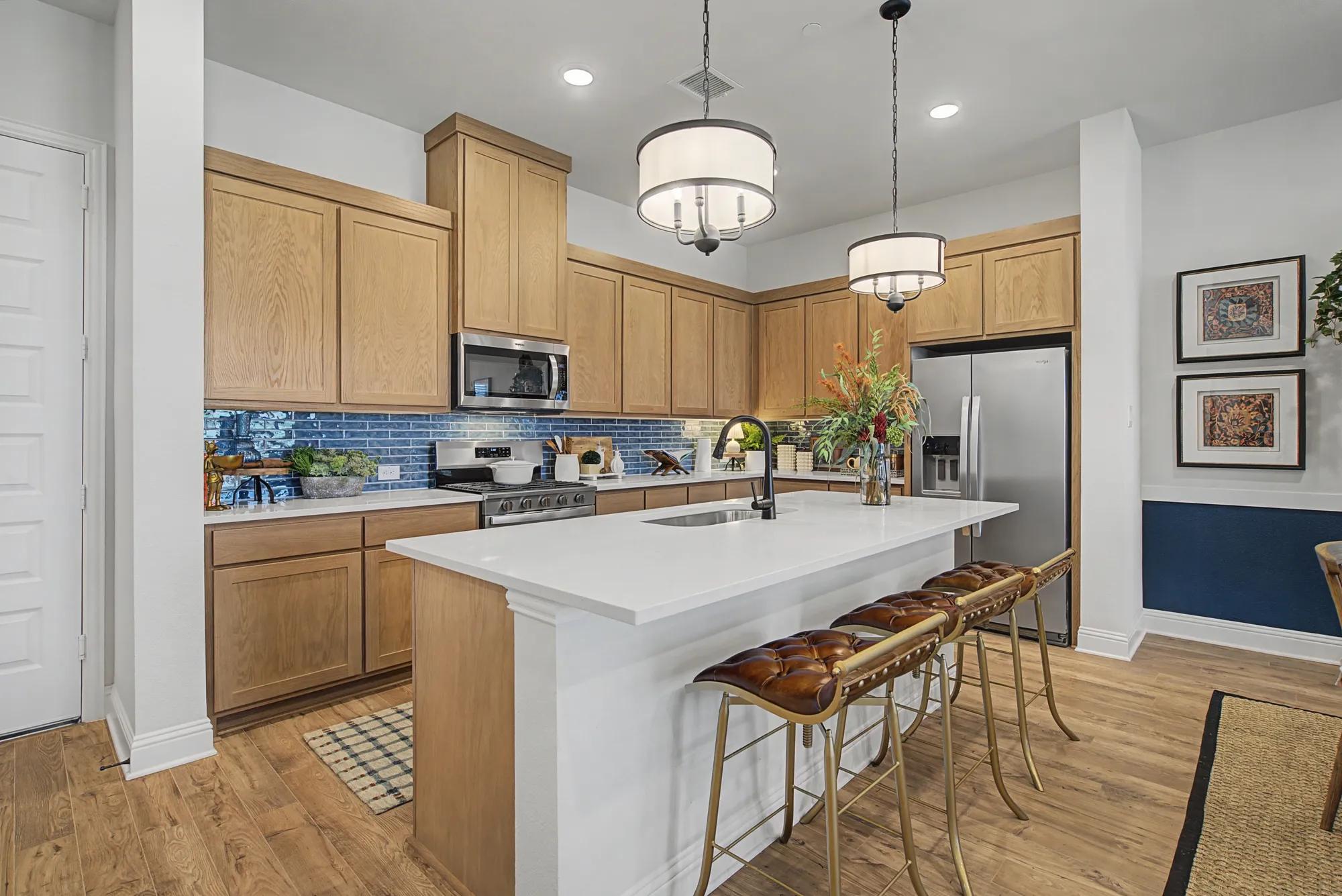 New townhome kitchen with light wood cabinets and blue tile backsplash 