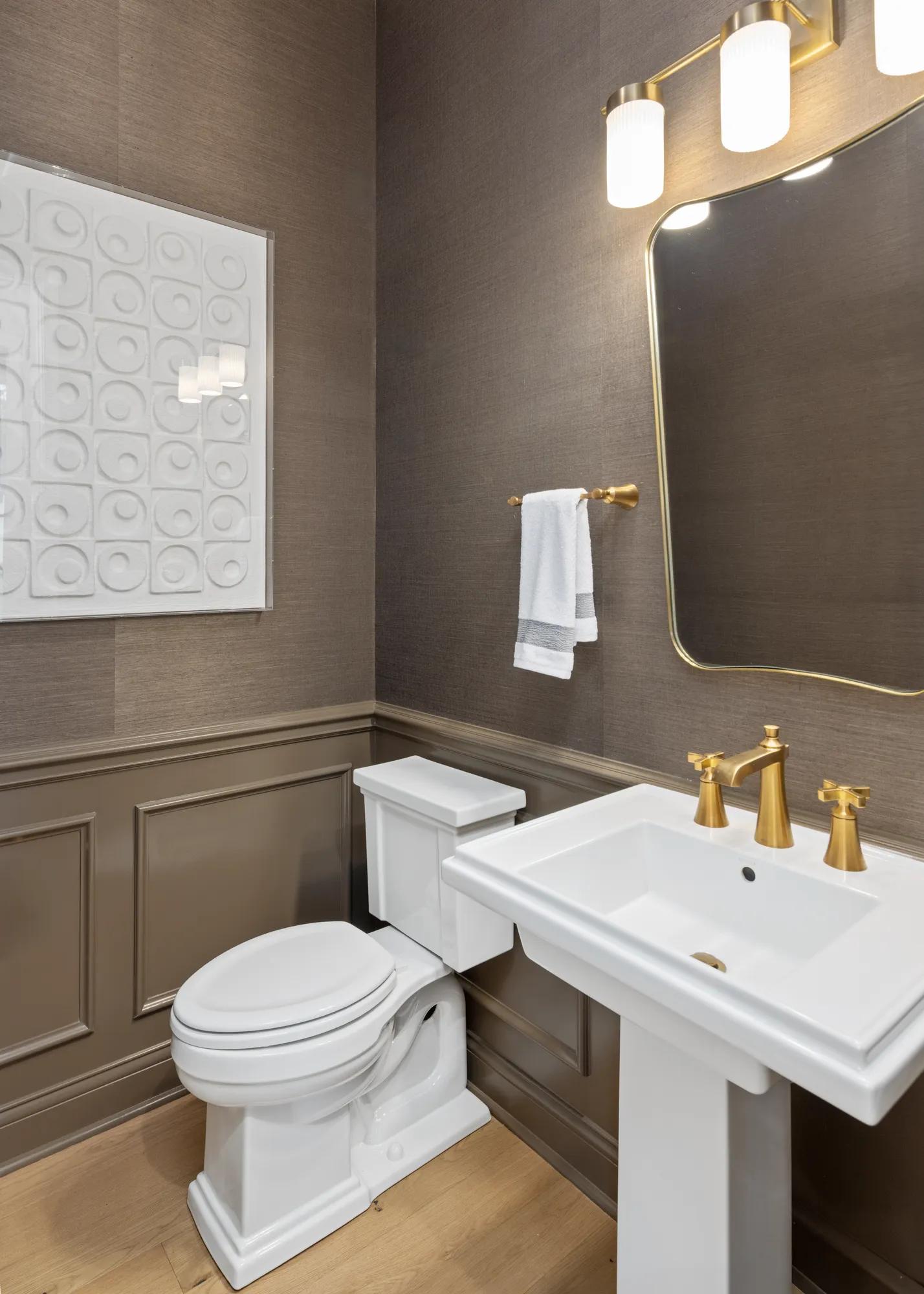 New home half bathroom with pedestal sink, gold finishes, brown wainscoting and wallpaper