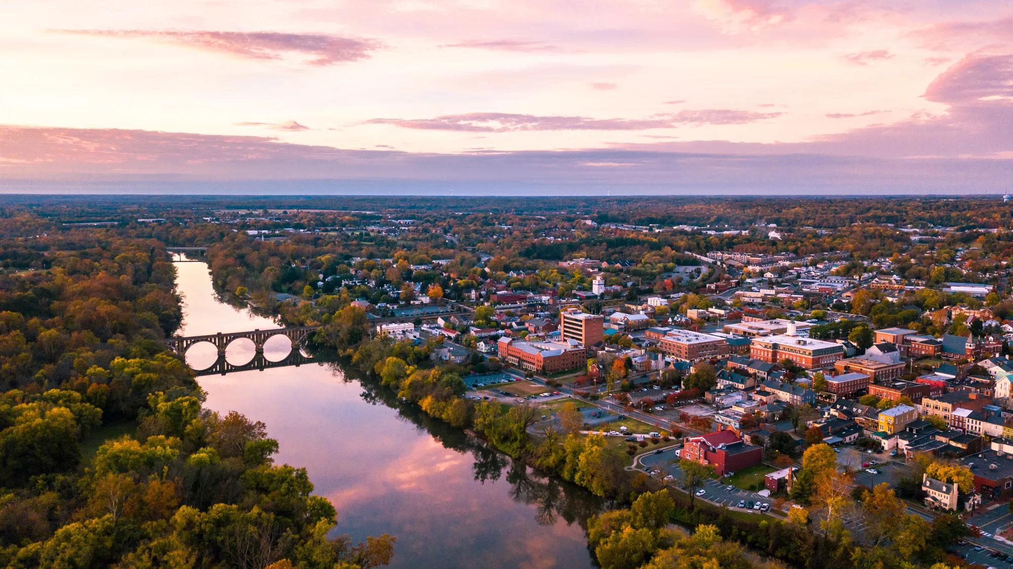 An aerial view of Fredericksburg, Virginia with the Rappahannock River in the foreground and the downtown area visible beyond at sunrise.