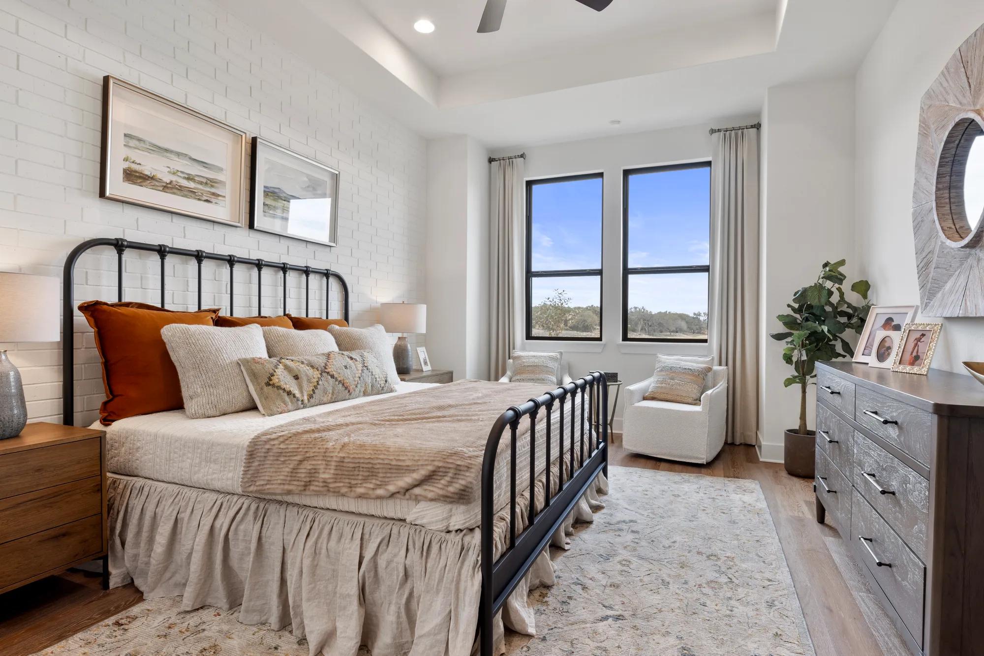 New home primary suite bedroom with white brick accent wall and hardwood floor