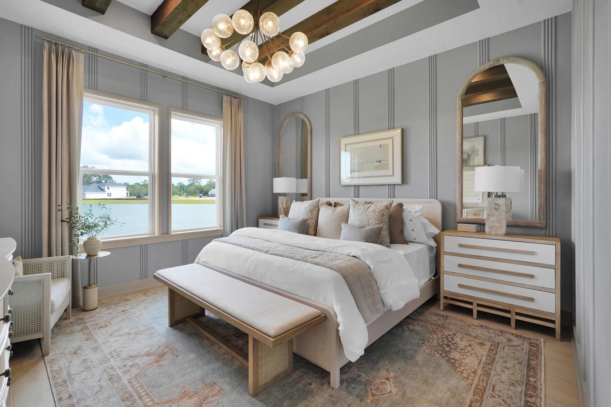 New home primary suite bedroom with gray accent walls and wood beam ceiling