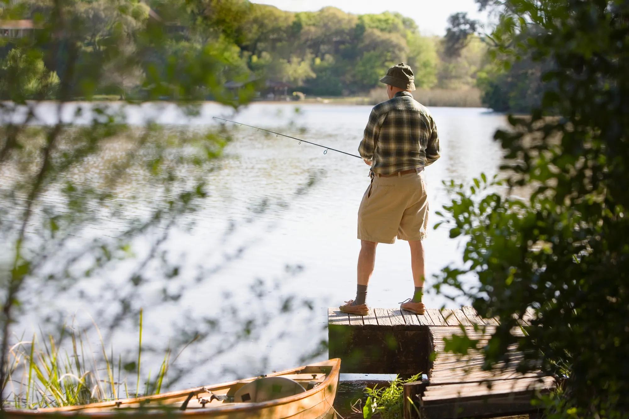 Man fishing off dock with small boat nearby